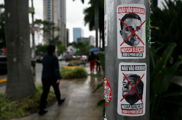 Posters bearing portraits of Brazil's Liberal Party (PL) presidential candidate Flavio Bolsonaro and US President Donald Trump crossed out with a red X are displayed on a utility pole in Sao Paulo, Brazil, on October 23, 2026. Brazil's President Lula da Silva and right-wing senator Flavio Bolsonaro head to a runoff election on October 25, a race that has become mired in allegations of social media malfeasance. (Photo by Juan Barreto / AFP)