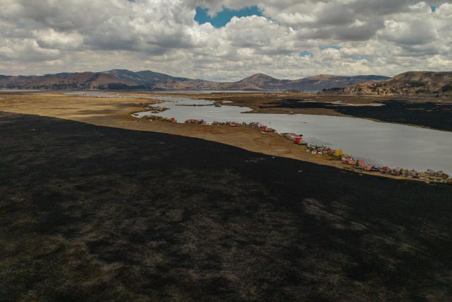 This aerial view shows a huge blackened area in the Lake Titicaca National Reserve near the floating islands of the Uros in Puno, Peru, on October 23, 2026, following a fire that ravaged around 400 hectares of totora reeds on October 21. Forest fires fueled by El Nino have killed 12 people and left hundreds homeless in Peru since June, authorities in the Andean country said on October 21. (Photo by URIEL MONTEFUR / AFP)