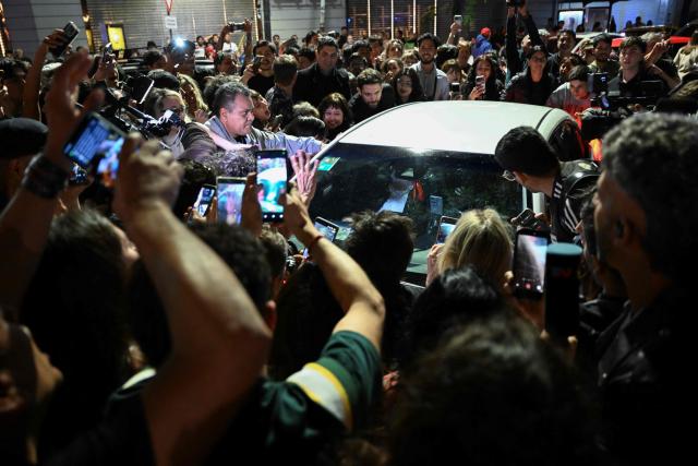 Fans of Argentina's music icon Charly Garcia surround his car outside his residence to celebrate his 75th birthday in Buenos Aires on October 23, 2026. (Photo by Luis ROBAYO / AFP)