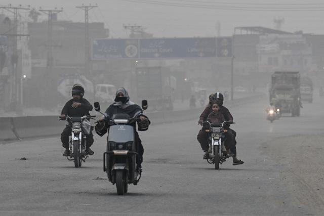 Commuters ride along a street amid smog in Lahore on October 24, 2026. (Photo by Arif ALI / AFP)