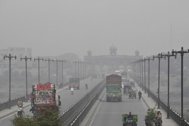 Commuters ride along a street amid smog in Lahore on October 24, 2026. (Photo by Arif ALI / AFP)