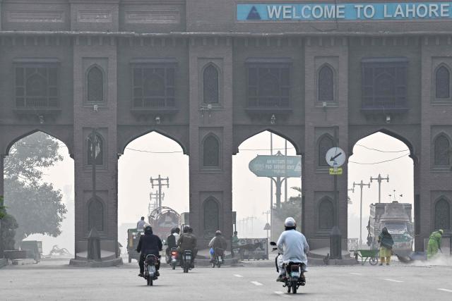 Commuters ride along a street amid smog in Lahore on October 24, 2026. (Photo by Arif ALI / AFP)
