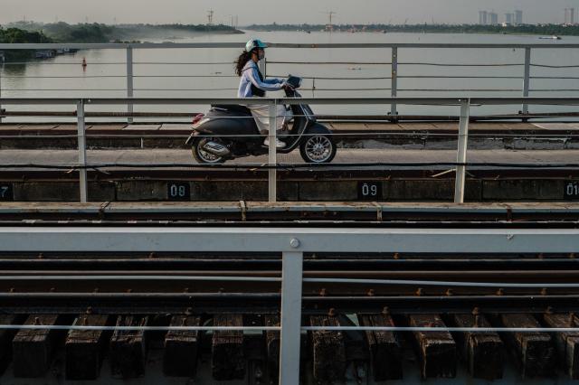 A motorist drives her motorbike on a bridge that runs over the Red River in Hanoi on October 23, 2026. (Photo by ANTHONY WALLACE / AFP)