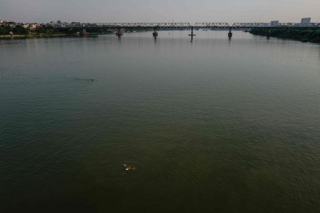 A swimmer (bottom) uses a makeshift inflatable buoy as he and other people swim in the waters of the Red River in Hanoi on October 23, 2026. (Photo by ANTHONY WALLACE / AFP)