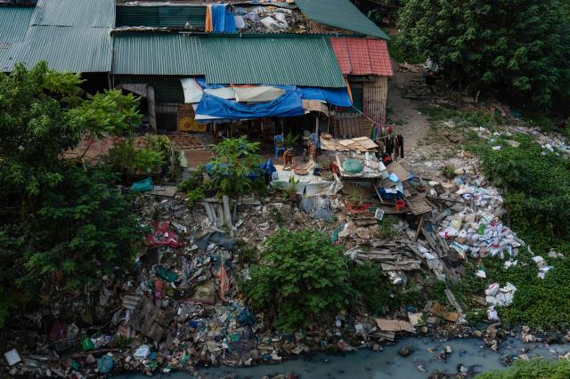 A resident (centre R) lays out food to dry outside her settlement near the Red River in Hanoi on October 23, 2026. (Photo by ANTHONY WALLACE / AFP)