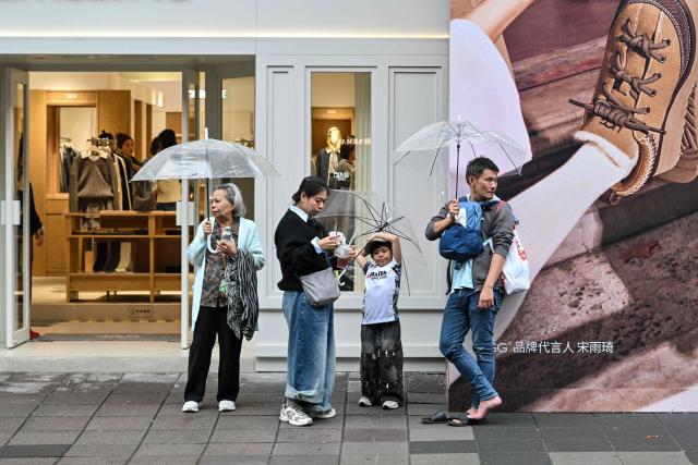 People stand next to a shop in the Xuhui district in Shanghai on October 24, 2026. (Photo by Hector RETAMAL / AFP)