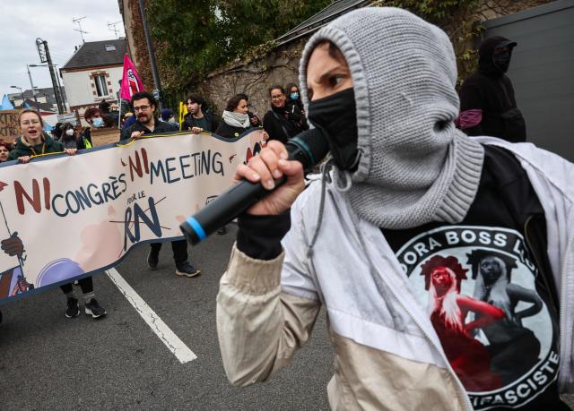 A protester speaks in a microphone as others hold a banner reading "neither congress nor meeting for the RN" during a demonstration "against racism, fascism and imperialism" on the sidelines of the Congress of the Far-right party Rassemblement National (RN) in Orleans, central France on October 24, 2026. Amid another Saturday of protests under tight security across France, Orleans is hosting the National congress of the Far-right party Rassemblement National and preparing for a record-breaking demonstration, on the eve of their first major campaign rally. (Photo by SIMON WOHLFAHRT / AFP)