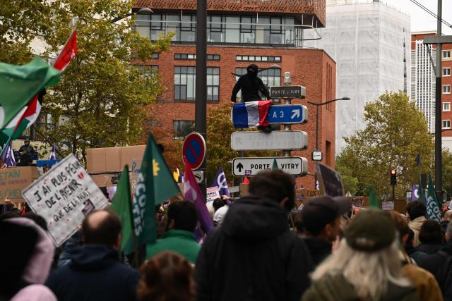 A protester holds a French flag bearing Gen Z sign during a demonstration in favor of purchasing power, the protection of public services, and fiscal and social justice, in Paris on October 24, 2026 as part of a nationwide call for mobilisation bringing together former members of the Yellow Vest movement, labor unions, high school and university students. Protests by high school students over learning conditions sparked a movement that has since spread nationwide, fuelled by broader anger over the rising cost of living. About 70,000 security personnel will be deployed on October 24, 2026, Interior Minister said at a news conference, warning that calls for violence and looting were circulating on social media. (Photo by Aris MESSINIS / AFP)