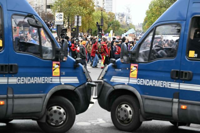 Protesters walk past gendarmerie vans during a demonstration in favor of purchasing power, the protection of public services, and fiscal and social justice, in Paris on October 24, 2026 as part of a nationwide call for mobilisation bringing together former members of the Yellow Vest movement, labor unions, high school and university students. Protests by high school students over learning conditions sparked a movement that has since spread nationwide, fuelled by broader anger over the rising cost of living. About 70,000 security personnel will be deployed on October 24, 2026, Interior Minister said at a news conference, warning that calls for violence and looting were circulating on social media. (Photo by NICOLAS TUCAT / AFP)