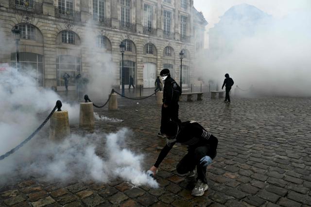 Protesters stand amid tear gas at Place de la Bourse, in a protest ban zone, as part of a demonstration in favor of purchasing power, the protection of public services, and fiscal and social justice, in Bordeaux, western France on October 24, 2026 as part of a nationwide call for mobilisation bringing together former members of the Yellow Vest movement, labor unions, high school and university students. Protests by high school students over learning conditions sparked a movement that has since spread nationwide, fuelled by broader anger over the rising cost of living. About 70,000 security personnel will be deployed on October 24, 2026, Interior Minister said at a news conference, warning that calls for violence and looting were circulating on social media. (Photo by Philippe LOPEZ / AFP)