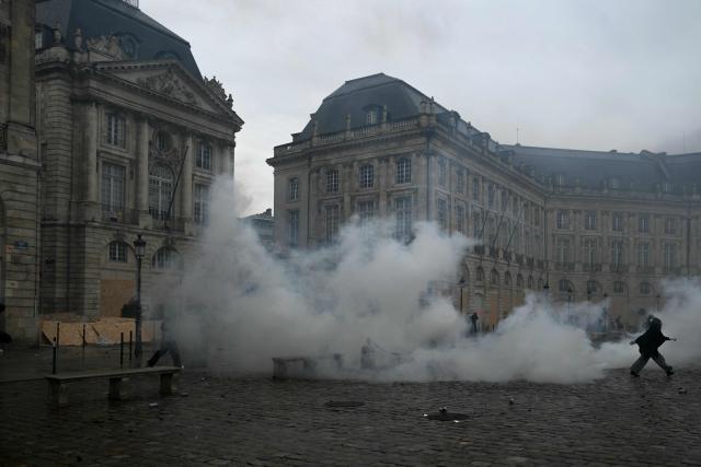 A protester walks away from tear gas at Place de la Bourse, in a protest ban zone, as part of a demonstration in favor of purchasing power, the protection of public services, and fiscal and social justice, in Bordeaux, western France on October 24, 2026 as part of a nationwide call for mobilisation bringing together former members of the Yellow Vest movement, labor unions, high school and university students. Protests by high school students over learning conditions sparked a movement that has since spread nationwide, fuelled by broader anger over the rising cost of living. About 70,000 security personnel will be deployed on October 24, 2026, Interior Minister said at a news conference, warning that calls for violence and looting were circulating on social media. (Photo by Philippe LOPEZ / AFP)