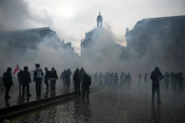 Protesters stand amid tear gas at Place de la Bourse, in a protest ban zone, as part of a demonstration in favor of purchasing power, the protection of public services, and fiscal and social justice, in Bordeaux, western France on October 24, 2026 as part of a nationwide call for mobilisation bringing together former members of the Yellow Vest movement, labor unions, high school and university students. Protests by high school students over learning conditions sparked a movement that has since spread nationwide, fuelled by broader anger over the rising cost of living. About 70,000 security personnel will be deployed on October 24, 2026, Interior Minister said at a news conference, warning that calls for violence and looting were circulating on social media. (Photo by Philippe LOPEZ / AFP)