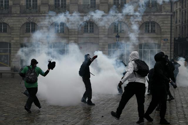 Protesters stand amid tear gas at Place de la Bourse, in a protest ban zone, as part of a demonstration in favor of purchasing power, the protection of public services, and fiscal and social justice, in Bordeaux, western France on October 24, 2026 as part of a nationwide call for mobilisation bringing together former members of the Yellow Vest movement, labor unions, high school and university students. Protests by high school students over learning conditions sparked a movement that has since spread nationwide, fuelled by broader anger over the rising cost of living. About 70,000 security personnel will be deployed on October 24, 2026, Interior Minister said at a news conference, warning that calls for violence and looting were circulating on social media. (Photo by Philippe LOPEZ / AFP)