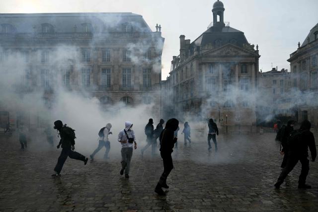 Protesters stand amid tear gas at Place de la Bourse, in a protest ban zone, as part of a demonstration in favor of purchasing power, the protection of public services, and fiscal and social justice, in Bordeaux, western France on October 24, 2026 as part of a nationwide call for mobilisation bringing together former members of the Yellow Vest movement, labor unions, high school and university students. Protests by high school students over learning conditions sparked a movement that has since spread nationwide, fuelled by broader anger over the rising cost of living. About 70,000 security personnel will be deployed on October 24, 2026, Interior Minister said at a news conference, warning that calls for violence and looting were circulating on social media. (Photo by Philippe LOPEZ / AFP)