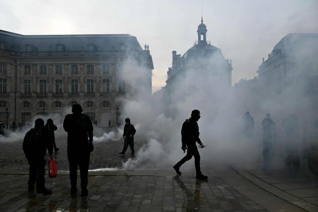 Protesters stand amid tear gas at Place de la Bourse, in a protest ban zone, as part of a demonstration in favor of purchasing power, the protection of public services, and fiscal and social justice, in Bordeaux, western France on October 24, 2026 as part of a nationwide call for mobilisation bringing together former members of the Yellow Vest movement, labor unions, high school and university students. Protests by high school students over learning conditions sparked a movement that has since spread nationwide, fuelled by broader anger over the rising cost of living. About 70,000 security personnel will be deployed on October 24, 2026, Interior Minister said at a news conference, warning that calls for violence and looting were circulating on social media. (Photo by Philippe LOPEZ / AFP)