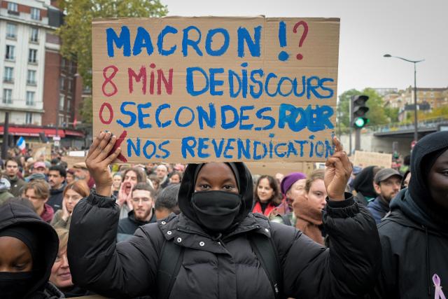 A protester holds a placard which reads "Macron's 8-minute speech, 0 seconds for our demands" during a demonstration in favor of purchasing power, the protection of public services, and fiscal and social justice, in Paris on October 24, 2026 as part of a nationwide call for mobilisation bringing together former members of the Yellow Vest movement, labor unions, high school and university students. Protests by high school students over learning conditions sparked a movement that has since spread nationwide, fuelled by broader anger over the rising cost of living. About 70,000 security personnel will be deployed on October 24, 2026, Interior Minister said at a news conference, warning that calls for violence and looting were circulating on social media. (Photo by DAMIEN MEYER / AFP)