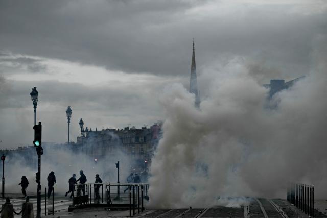 Protesters stand amid tear gas near Place de la Bourse, in a protest ban zone, as part of a demonstration in favor of purchasing power, the protection of public services, and fiscal and social justice, in Bordeaux, western France on October 24, 2026 as part of a nationwide call for mobilisation bringing together former members of the Yellow Vest movement, labor unions, high school and university students. Protests by high school students over learning conditions sparked a movement that has since spread nationwide, fuelled by broader anger over the rising cost of living. About 70,000 security personnel will be deployed on October 24, 2026, Interior Minister said at a news conference, warning that calls for violence and looting were circulating on social media. (Photo by Philippe LOPEZ / AFP)