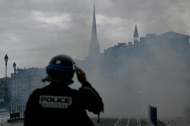 A police officer stands amid tear gas during a demonstration in favor of purchasing power, the protection of public services, and fiscal and social justice, in Bordeaux, western France on October 24, 2026 as part of a nationwide call for mobilisation bringing together former members of the Yellow Vest movement, labor unions, high school and university students. Protests by high school students over learning conditions sparked a movement that has since spread nationwide, fuelled by broader anger over the rising cost of living. About 70,000 security personnel will be deployed on October 24, 2026, Interior Minister said at a news conference, warning that calls for violence and looting were circulating on social media. (Photo by Philippe LOPEZ / AFP)