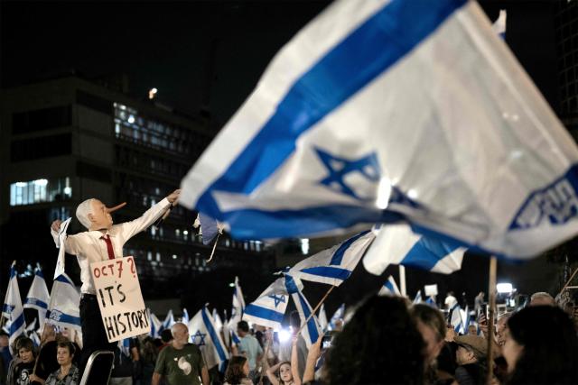 A protester wearing a mask depicting Israeli Prime Minister Benjamin Netanyahu with an elongated nose, evoking the literary character Pinocchio, poses with a placard during an anti-government demonstration at the Hostages Square in Tel Aviv on October 24, 2026, ahead of Israel's legislative election. (Photo by Jewel SAMAD / AFP)