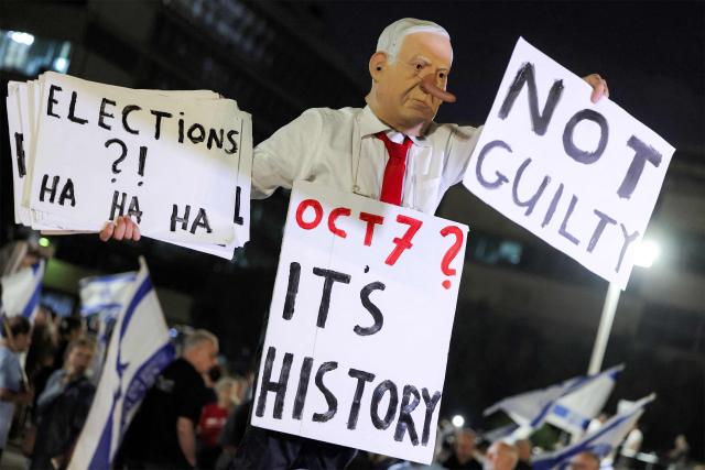 A protester wearing a mask depicting Israeli Prime Minister Benjamin Netanyahu with an elongated nose, evoking the literary character Pinocchio, poses with a placard during an anti-government demonstration at the Hostages Square in Tel Aviv on October 24, 2026, ahead of Israel's legislative election. (Photo by Jack GUEZ / AFP)