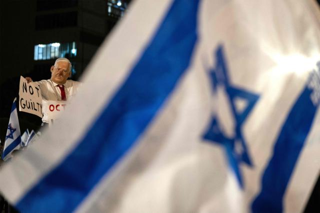 A protester wearing a mask depicting Israeli Prime Minister Benjamin Netanyahu with an elongated nose, evoking the literary character Pinocchio, poses with a placard during an anti-government demonstration at the Hostages Square in Tel Aviv on October 24, 2026, ahead of Israel's legislative election. (Photo by Jewel SAMAD / AFP)