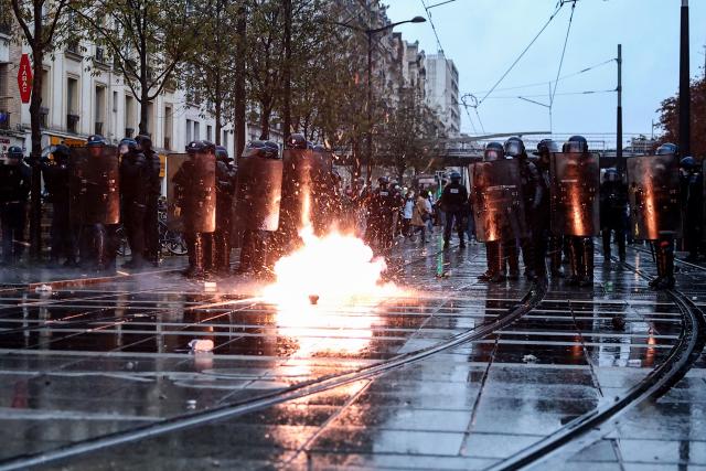 French Police officers in riot gear (L) and French Gendarmes stand guard as tear gas cansiter explodes during a demonstration in favor of purchasing power, the protection of public services, and fiscal and social justice, in Paris on October 24, 2026 as part of a nationwide call for mobilisation bringing together former members of the Yellow Vest movement, labor unions, high school and university students. Protests by high school students over learning conditions sparked a movement that has since spread nationwide, fuelled by broader anger over the rising cost of living. About 70,000 security personnel will be deployed on October 24, 2026, Interior Minister said at a news conference, warning that calls for violence and looting were circulating on social media. (Photo by Sameer AL-DOUMY / AFP)