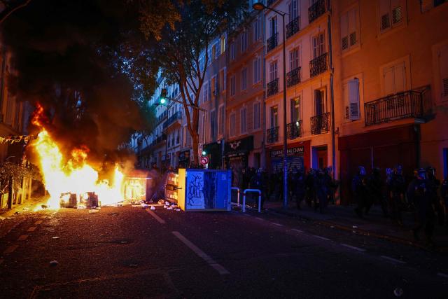 French riot police walk past a burning barricade during a demonstration in favor of purchasing power, the protection of public services, and fiscal and social justice, in Marseille, southeastern France on October 24, 2026 as part of a nationwide call for mobilisation bringing together former members of the Yellow Vest movement, labor unions, high school and university students. Protests by high school students over learning conditions sparked a movement that has since spread nationwide, fuelled by broader anger over the rising cost of living. About 70,000 security personnel will be deployed on October 24, 2026, Interior Minister said at a news conference, warning that calls for violence and looting were circulating on social media. (Photo by Thibaud MORITZ / AFP)