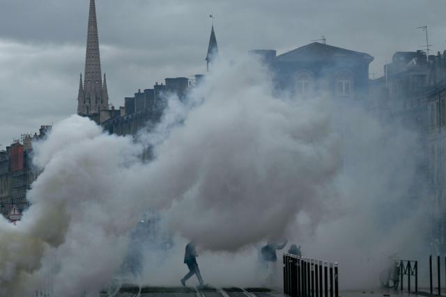 Protesters stand amid tear gas near Place de la Bourse, in a protest ban zone, as part of a demonstration in favor of purchasing power, the protection of public services, and fiscal and social justice, in Bordeaux, western France on October 24, 2026 as part of a nationwide call for mobilisation bringing together former members of the Yellow Vest movement, labor unions, high school and university students. Protests by high school students over learning conditions sparked a movement that has since spread nationwide, fuelled by broader anger over the rising cost of living. About 70,000 security personnel will be deployed on October 24, 2026, Interior Minister said at a news conference, warning that calls for violence and looting were circulating on social media. (Photo by Philippe LOPEZ / AFP)