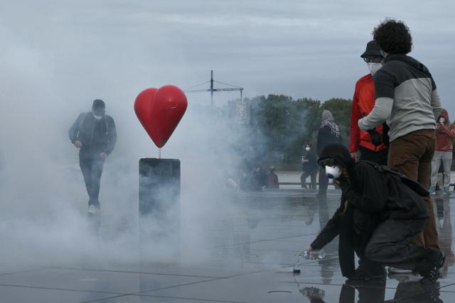 Protesters stand amid tear gas near Place de la Bourse, in a protest ban zone, as part of a demonstration in favor of purchasing power, the protection of public services, and fiscal and social justice, in Bordeaux, western France on October 24, 2026 as part of a nationwide call for mobilisation bringing together former members of the Yellow Vest movement, labor unions, high school and university students. Protests by high school students over learning conditions sparked a movement that has since spread nationwide, fuelled by broader anger over the rising cost of living. About 70,000 security personnel will be deployed on October 24, 2026, Interior Minister said at a news conference, warning that calls for violence and looting were circulating on social media. (Photo by Philippe LOPEZ / AFP)