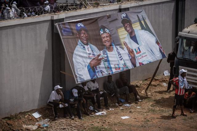 Supporters of the All Progressives Congress (APC) takes shelter under a campaign banner during the presidential campaign flag-off rally at the Ranchers Bees stadium in Kaduna, on October 24, 2026. Nigerian President Bola Tinubu launches his re-election campaign on Saturday facing voter anger over insecurity and economic hardships. (Photo by Light Oriye Tamunotonye / AFP)