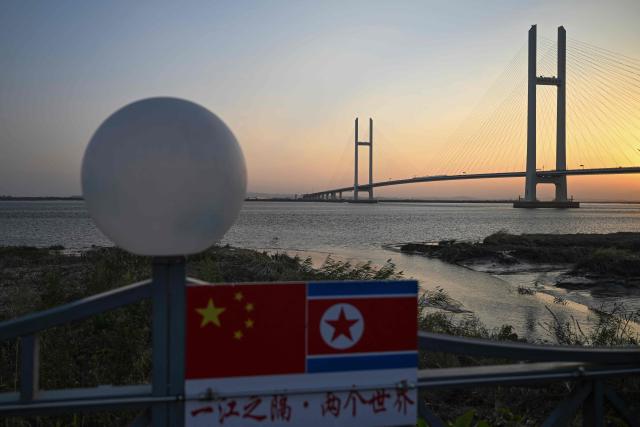 Chinese and North Korean flags are seen at a lookout area in Dandong, in northeastern China's Liaoning province, as the new cross-border bridge linking China and North Korea (background) is seen at sunrise on October 25, 2026. North Korean leader Kim Jong Un returned home October 24 after a day-long trip to the Chinese border city of Dandong, Beijing's state media reported, though the purpose of the unannounced visit was not immediately clear. (Photo by Pedro PARDO / AFP)