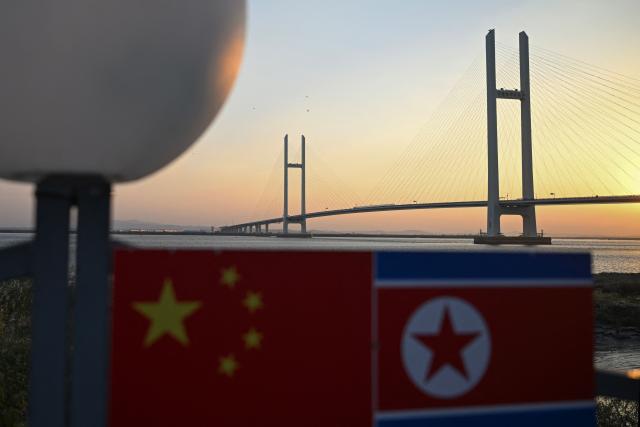 Chinese and North Korean flags are seen at a lookout area in Dandong, in northeastern China's Liaoning province, as the new cross-border bridge linking China and North Korea (background) is seen at sunrise on October 25, 2026. North Korean leader Kim Jong Un returned home October 24 after a day-long trip to the Chinese border city of Dandong, Beijing's state media reported, though the purpose of the unannounced visit was not immediately clear. (Photo by Pedro PARDO / AFP)