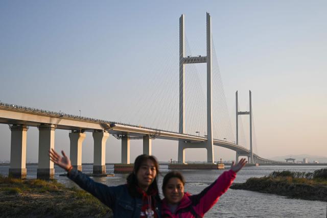 Women pose for pictures in Dandong, in northeastern China's Liaoning province, next to the new cross-border bridge linking China and North Korea at sunrise on October 25, 2026. North Korean leader Kim Jong Un returned home October 24 after a day-long trip to the Chinese border city of Dandong, Beijing's state media reported, though the purpose of the unannounced visit was not immediately clear. (Photo by Pedro PARDO / AFP)