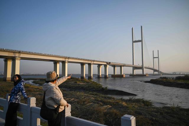 People look on in Dandong, in northeastern China's Liaoning province, next to the new cross-border bridge linking China and North Korea at sunrise on October 25, 2026. North Korean leader Kim Jong Un returned home October 24 after a day-long trip to the Chinese border city of Dandong, Beijing's state media reported, though the purpose of the unannounced visit was not immediately clear. (Photo by Pedro PARDO / AFP)