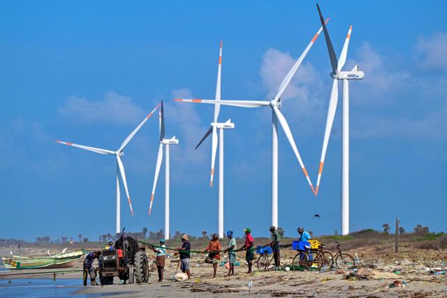 This photograph taken on October 3, 2026 shows fishermen catching fish at a beach near a wind power plant in Sri Lanka's Mannar Peninsula. The government aims to generate 70 percent of the country's electricity from renewable sources by 2030, including wind power. But it has frozen new projects in Mannar to ease local opposition. Since they appeared six years ago, the Mannar wind turbines have been blamed for a host of problems -- from dwindling catches to floods, fuelling opposition to green energy projects as fuel costs soar. (Photo by Ishara S. KODIKARA / AFP)