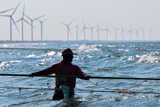 This photograph taken on October 3, 2026 shows a fisherman catching fish at a beach near a wind power plant in Sri Lanka's Mannar Peninsula. The government aims to generate 70 percent of the country's electricity from renewable sources by 2030, including wind power. But it has frozen new projects in Mannar to ease local opposition. Since they appeared six years ago, the Mannar wind turbines have been blamed for a host of problems -- from dwindling catches to floods, fuelling opposition to green energy projects as fuel costs soar. (Photo by Ishara S. KODIKARA / AFP)