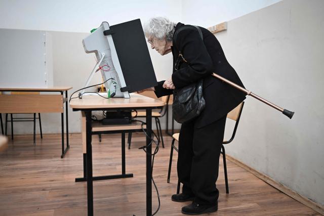 An elderly woman uses a voting booth machine to cast her vote for the Bulgaria's presidential election at a polling station in Sofia on October 25, 2026. Bulgarians are voting in a presidential election on October 25, as security concerns swirl following a series of drone attacks on ships in the Black Sea. The incumbent President, who favors dialogue with Moscow and opposes military aid to Ukraine, is the frontrunner for a new term in the largely ceremonial post, polls show. (Photo by Nikolay DOYCHINOV / AFP)