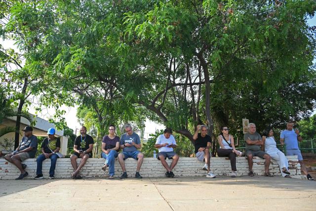 People wait for the polls to open sitting on a wall during the presidential election runoff in Brasilia, Brazil, on October 25, 2026. Brazilians head to the polls for a runoff between President Luiz Inacio Lula da Silva and right-wing senator Flavio Bolsonaro that will determine whether Brazil remains one of the few leftist nations in the region or joins a regional swing to the right championed by US President Donald Trump, a Bolsonaro ally. (Photo by Evaristo SA / AFP)