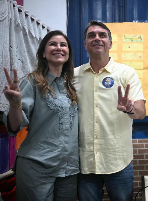Brazil's right-wing senator and Liberal Party (PL) presidential candidate Flavio Bolsonaro and his wife Fernanda Bolsonaro make V-for-victory signs during the presidential runoff election at a polling station in Rio de Janeiro, Brazil, on October 25, 2026. Flavio Bolsonaro faces President Luiz Inacio Lula da Silva in a runoff that will determine whether Brazil remains one of the few leftist nations in the region or joins a regional swing to the right championed by his ally, US President Donald Trump. (Photo by MAURO PIMENTEL / AFP)