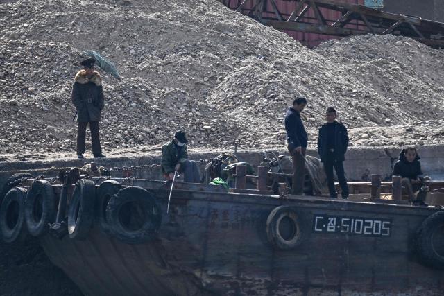 A North Korean soldier (L) and men are seen on the waterfront of the Yalu River in the North Korean town of Sinuiju, viewed from the border city of Dandong, in China's northeast Liaoning province, on October 25, 2026.  (Photo by Pedro PARDO / AFP)