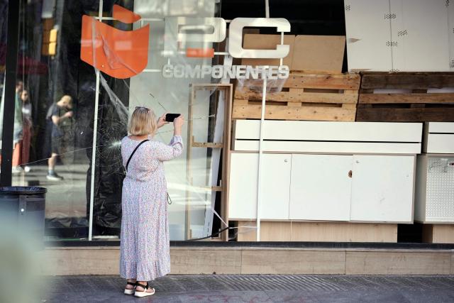 A woman takes images of an electronics store looted the previous night during riots, in Barcelona on October 25, 2026. Police made 128 arrests overnight in Barcelona for acts of "vandalism", damage to public property" and "looting", the regional Catalan police said today. Seventy-three of those arrested were minors, with the reports due to be sent "to the juvenile prosecutor's office", Catalan police chief Silvia Cata told Spain's 3CatInfo media outlet. (Photo by Manaure QUINTERO / AFP)
