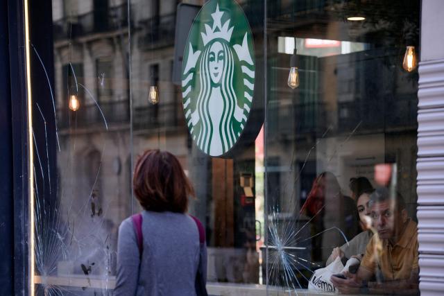 Costumers look through the broken windows of a coffe shop damaged the previous night during riots, in Barcelona on October 25, 2026. Police made 128 arrests overnight in Barcelona for acts of "vandalism", damage to public property" and "looting", the regional Catalan police said today. Seventy-three of those arrested were minors, with the reports due to be sent "to the juvenile prosecutor's office", Catalan police chief Silvia Cata told Spain's 3CatInfo media outlet. (Photo by Manaure QUINTERO / AFP)
