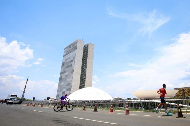 A cyclist and a runner pass in front of the National Congress building in Brasilia, Brazil, on October 25, 2026, during the presidential runoff election. Brazilians head to the polls for a runoff between President Luiz Inacio Lula da Silva and right-wing senator Flavio Bolsonaro that will determine whether Brazil remains one of the few leftist nations in the region or joins a regional swing to the right championed by US President Donald Trump, a Bolsonaro ally. (Photo by Igo ESTRELA / AFP)