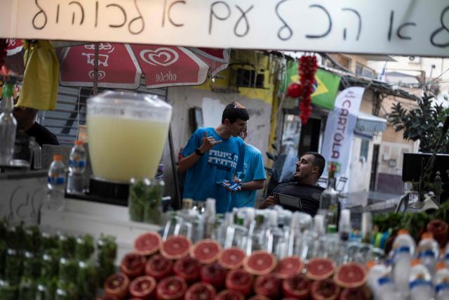 HaDemokratim (The Democrats) party leader Yair Golan's supporters speak with a vendor as they campaign in a market area in Tel Aviv on October 25, 2026, ahead of Israel's legislative election. Israel heads to the polls on October 27 in its first election since the October 7, 2023 Hamas-led attack, in what is seen as a referendum on the prime minister. (Photo by Jewel SAMAD / AFP)
