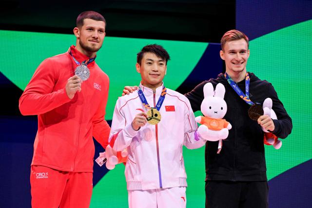 (From L) Silver medallist Croatia's Illia Kovtun, gold medallist China's Jingyuan Zou and bronze medallist Individual Neutral Athlete Daniel Marinov celebrate on the podium after the Men's Parallel Bars Final during the 54th FIG Artistic Gymnastics World Championships, in Rotterdam, southern Netherlands, on October 25, 2026. (Photo by JOHN THYS / AFP)