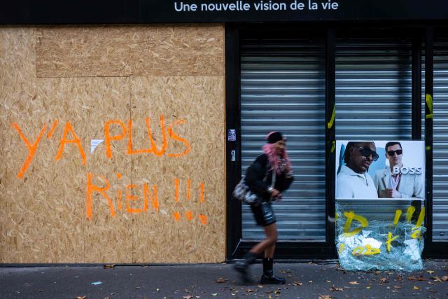 A woman walks past an optician’s shattered shop window covered by a wooden board with the words "there’s nothing left" written on, in Paris on October 25, 2026. (Photo by JOEL SAGET / AFP)