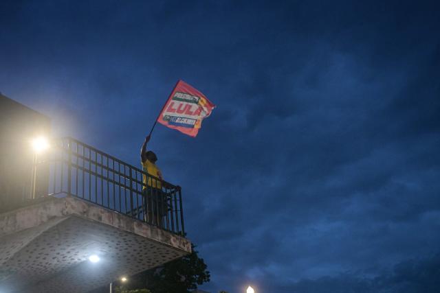 A supporter of Brazilian President and Workers´ Party (PT) re-election candidate Luiz Inacio Lula da Silva waves a flag in Belo Horizonte, Brazil, on October 25, 2026, the day of the presidential runoff election. Lula da Silva faces right-wing senator Flavio Bolsonaro in a runoff that will determine whether Brazil remains one of the few leftist nations in the region or joins a regional swing to the right championed by US President Donald Trump, Bolsonaro's ally. (Photo by Daniel DE CERQUEIRA / AFP)