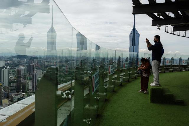 A tourist takes photos of the city skyline as haze conditions due to Indonesian wildfires improve in Kuala Lumpur on October 26, 2026. The haze has sent air pollution levels surging to dangerous levels not only in Indonesia, but also in Malaysia, Singapore and East Timor, prompting the ASEAN regional bloc to call a meeting over the crisis. (Photo by Mohd Rasfan / AFP)