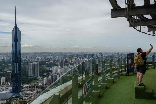 A tourist takes a selfie with the city skyline seen in the background as haze conditions due to Indonesian wildfires improve in Kuala Lumpur on October 26, 2026. The haze has sent air pollution levels surging to dangerous levels not only in Indonesia, but also in Malaysia, Singapore and East Timor, prompting the ASEAN regional bloc to call a meeting over the crisis. (Photo by Mohd Rasfan / AFP)