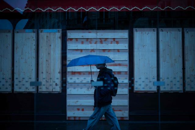 A passer-by walks past a closed shop protected with wooden panels in Paris on 24 October, 2026, on the day of nationwide protests bringing together former members of the Yellow Vest movement, labor unions, high school and university students. Protests by high school students over learning conditions sparked a movement that has since spread nationwide, fuelled by broader anger over the rising cost of living. About 70,000 security personnel will be deployed on October 24, 2026, Interior Minister said at a news conference, warning that calls for violence and looting were circulating on social media. (Photo by Olivier MORIN / AFP)